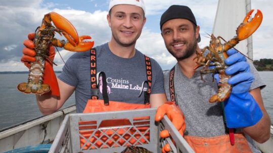 Two people holding lobsters in hands on a boat